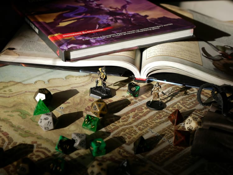 A variety of polyhedral dice and miniatures scattered over a game map. Two game books are placed in the background.