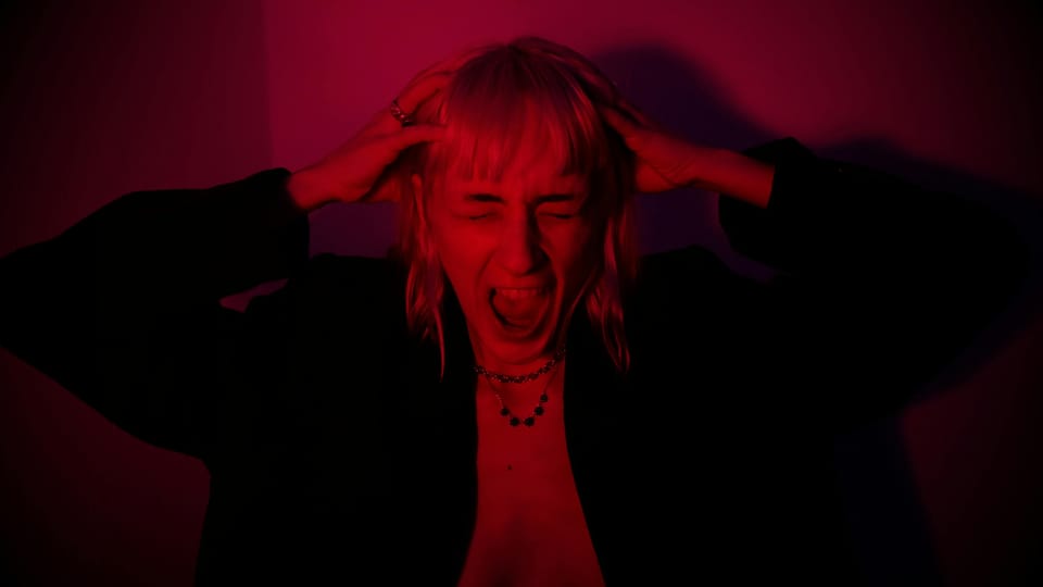 A long-haired woman screaming, pressing her hands to her head in frustration.